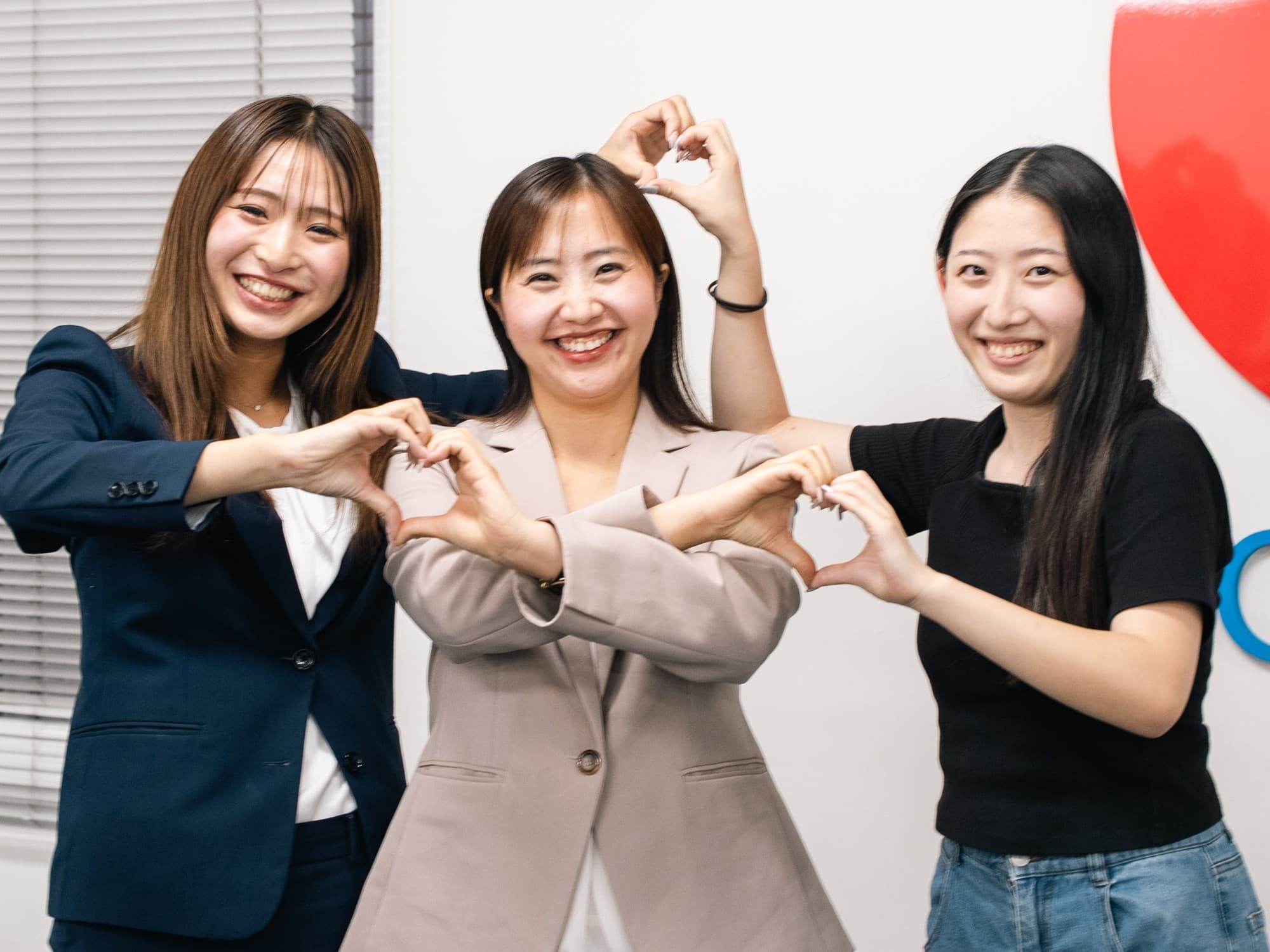 笑顔でハートのポーズをつくる3人のメンバー